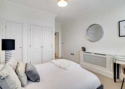 Professionally staged home by Beau Property Home Staging. Show home bedroom featuring radiator cover, plants, mirror and staged bed