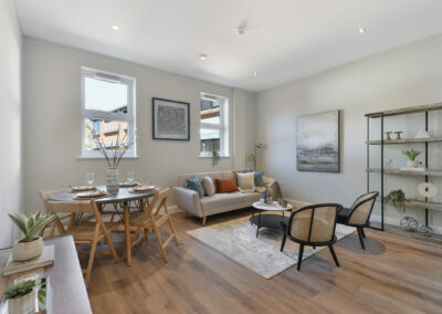 Professionally staged home by Beau Property Home Staging. Show home lounge/diner featuring coffee table, set dining table, shelving, plants, hanging artwork