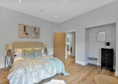 Professionally staged home by Beau Property Home Staging. Show home bedroom featuring staged bed with decorative cushions and pillows, mirror, small chest of drawers