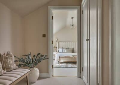Open doorway looking into a staged bedroom of Hungershall Mews in Tunbridge Wells. Cream coloured double bed with large headboard featuring decorative throw & pillows. Decorative plants added for extra detail and homely feel.